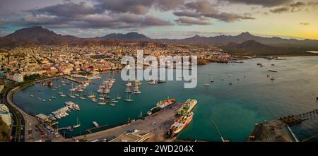 Panoramablick auf die Stadt Mindelo bei Sonnenuntergang, mit dem Yachthafen und Booten im Vordergrund, umgeben von der pulsierenden Stadtlandschaft und den Bergen im Stockfoto