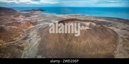 Luftaufnahme einer vulkanischen Küstenlandschaft (Vulkan Viana, Sao Vicente) mit einem markanten Krater im Vordergrund, karger Vegetation und einer kleinen Ville Stockfoto