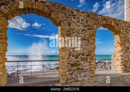 Wellen, die auf die Felsen stürzen, von einem Steinbogen auf dem Pier von Cefalù, Sizilien aus gesehen Stockfoto