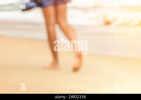 Unfokussierte weibliche Füße, die auf dem Sand laufen. Sandstrand während der goldenen Stunde des Sonnenuntergangs Stockfoto