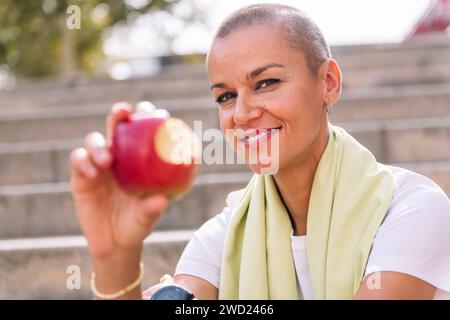 Lächelnde Sportfrau zeigt einen gebissenen Apfel Stockfoto