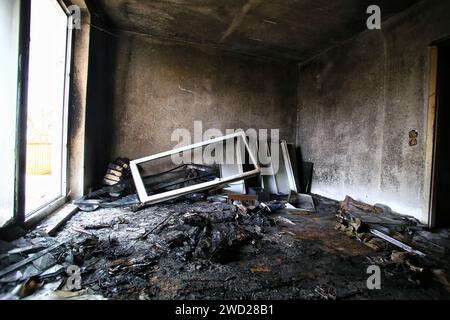 Verbranntes und zerstörtes Zimmer mit hellem Tageslicht von der Balkontür. Stockfoto