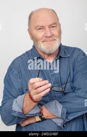 Porträt eines attraktiven grauhaarigen Mannes in einem Jeanshemd isoliert auf grauem Hintergrund. Bärtiger Großvater europäischer Art. Stockfoto