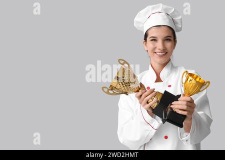 Weibliche Köchin mit goldenen Tassen auf hellem Hintergrund Stockfoto