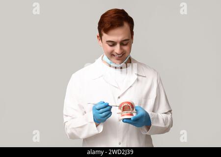 Männlicher Zahnarzt mit Zahnforscher und Kiefermodell auf grauem Hintergrund. Weltzahnarzttag Stockfoto