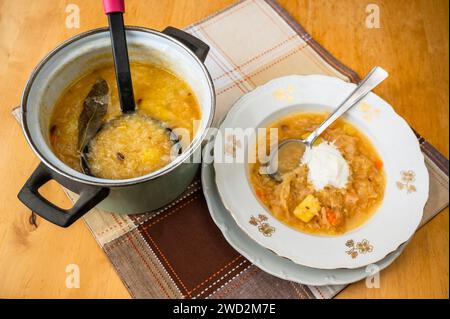 Kohlsuppe mit Kartoffeln im Zierteller und im Topf mit Schöpflöffel, Tischdecke auf Tisch, Nahaufnahme. Stockfoto