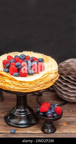 Stapel traditioneller Crepes auf hölzernem Hintergrund mit frischen Beeren auf der Oberseite. Maslenitsa traditionelle russische Festmahlzeit. Stockfoto