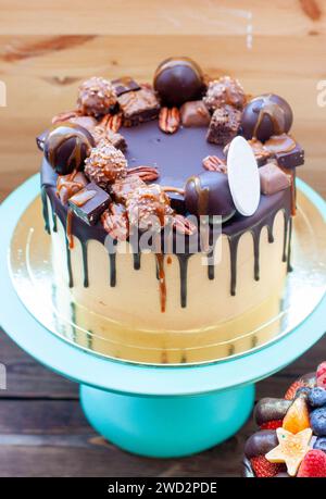 Schokoladenkuchen mit Trüffeln, Süßigkeiten, Keksen, Pekannüssen mit geschmolzener Schokolade und gesalzenem Karamell auf der Oberseite Stockfoto