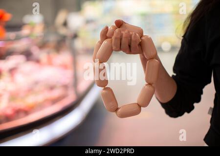 Hände, die einen Haufen Würstchen vor dem Hintergrund einer verschwommenen Ladentheke halten. Stockfoto