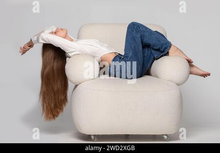 Ein schönes, schlankes Mädchen mit langen blonden Haaren liegt in einem bequemen, weißen Stuhl. Eine Frau ruht und entspannt sich in einem Stuhl. Stockfoto