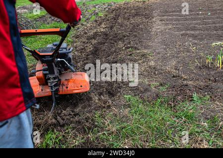 Der Landwirt nutzt einen leistungsstarken Motorgrubber, um den Boden auf dem Land zu pflegen und ihn für die bevorstehende Frühjahrssaat vorzubereiten. Stockfoto