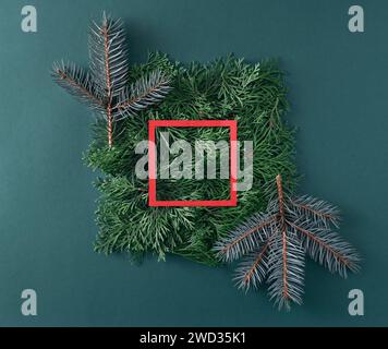 Weihnachtsbaum und Thuja-Zweige mit rotem Papierrahmen auf grünem Hintergrund. Kreatives Konzept des Urlaubs in minimalem Stil. Stockfoto