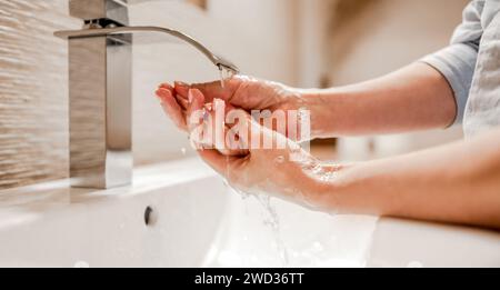 Ein Mädchen wäscht sich die Hände mit Seifenschaum im Badezimmer mit einem Stahlhahn. Hygiene und Reinigungsverfahren zur Vorbeugung gegen Viren und Leiden Stockfoto