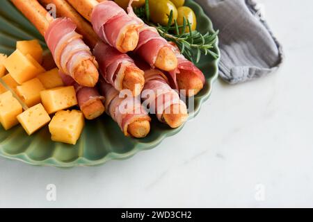 Schinkenscheiben oder Marmeladen. Köstliche grissini-Sticks mit Schinken, Käse, Rosmarin, Oliven auf grüner Platte auf dunklem Hintergrund. Vorspeisentisch Stockfoto