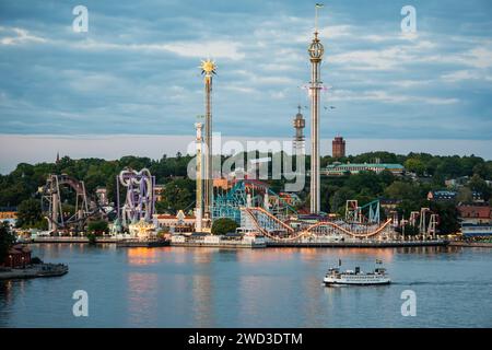 Abendlicher Blick auf den Vergnügungspark Gröna Lund in Stockholm, im Sommer. Teilweise bewölkter Himmel, farbenfroher Abend. Eine Pendlerfähre fährt vorbei. Stockfoto