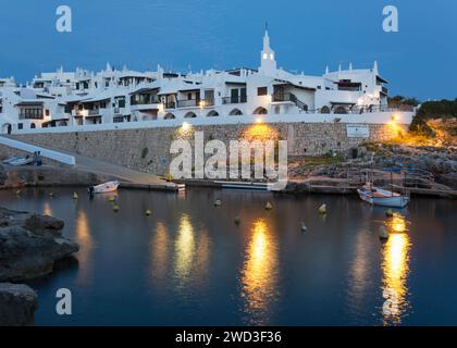 Binibèquer Vell, Menorca, Balearen, Spanien. Beleuchteter Hafen und weiße Dorfhäuser in der Abenddämmerung. Stockfoto