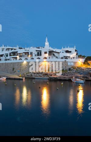 Binibèquer Vell, Menorca, Balearen, Spanien. Beleuchteter Hafen und weiße Dorfhäuser in der Abenddämmerung. Stockfoto