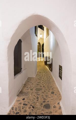 Binibèquer Vell, Menorca, Balearen, Spanien. Beleuchtete Straße zwischen weißen Dorfhäusern bei Nacht. Stockfoto