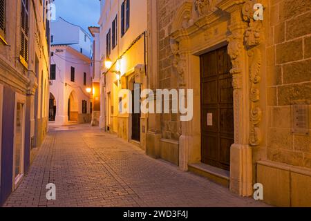 Ciutadella, Menorca, Balearen, Spanien. Blick auf die beleuchtete Altstadtstraße, Sonnenaufgang, die Kirchentür ist deutlich sichtbar. Stockfoto