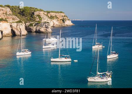 Cala Galdana, Menorca, Balearen, Spanien. Blick auf das ruhige blaue Wasser von Cala Macarella, Yachten vor der Küste vor Anker. Stockfoto