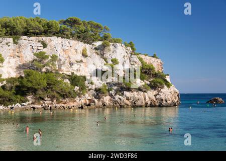 Cala Galdana, Menorca, Balearen, Spanien. Blick über das türkisfarbene Wasser von Cala Macarella zu Kiefern bewachsenen Kalksteinklippen. Stockfoto