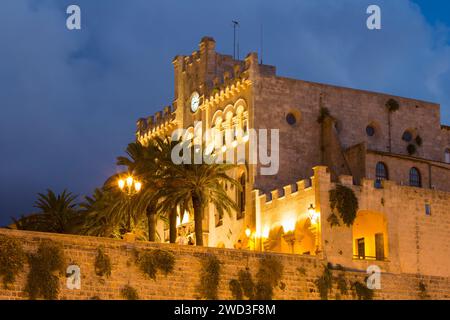 Ciutadella, Menorca, Balearen, Spanien. Flacher Blick auf das beleuchtete Rathaus aus aus dem 19. Jahrhundert auf der Plac d'es Born, Abenddämmerung. Stockfoto