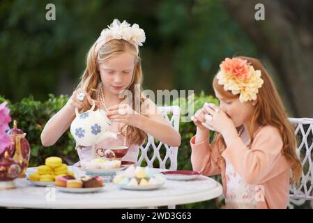 Mädchen, Kinder und Teeparty oder Outdoor-Spaß für Fantasy-Spiele im Garten für Kuchen-Snack, Geburtstag oder Spiel. Kinder, Schwestern und schicke Kostüme in der Natur Stockfoto