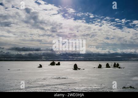 Silhouetten von Fischern und Schneemobil im Winter auf dem Eis des Flusses unter dem blauen bewölkten Himmel frostiger Tag Stockfoto