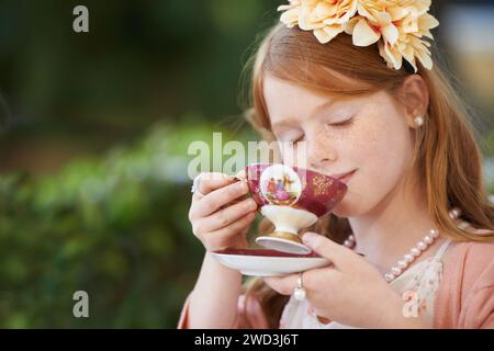 Mädchen, Kind und trinken Tee im Garten mit Party zum Geburtstag, Feiern und Spielen im Freien zu Hause. Person, Kind und Porzellanbecher im Hinterhof Stockfoto