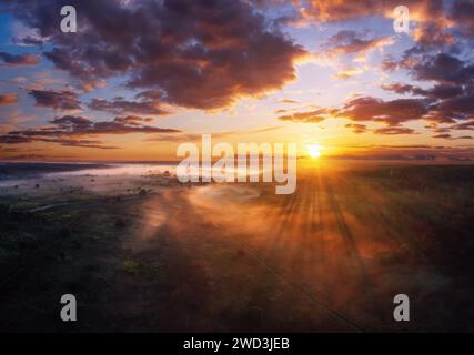 Farbenfrohe Morgenlandschaft mit dramatischem Himmel über dem nebeligen Feld bei Sonnenuntergang aus der Vogelperspektive. Stockfoto