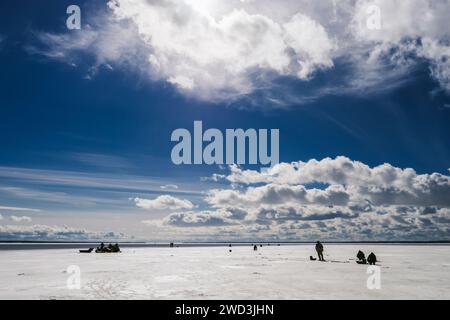 Silhouetten von Fischern und Schneemobil im Winter auf dem Eis des Flusses unter dem blauen bewölkten Himmel frostiger Tag Stockfoto