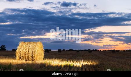Abendliche Heuhüpflandschaft auf dem Feld. Der Stapel wird durch einen Blitz beleuchtet. Stockfoto