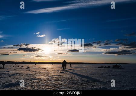 Silhouetten einer Gruppe von Fischern auf dem Eis des Sees am Morgen gegen den schönen Sonnenaufgang Stockfoto