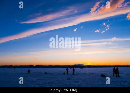 Silhouetten männlicher Fischer beim Winterfischen auf dem Eis des Flusses am Abend gegen Sonnenuntergang Stockfoto