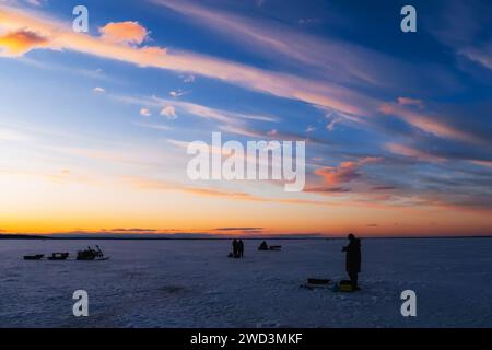 Silhouetten eines Fischers mit Angelrute an einem frostigen Winterabend bei Sonnenuntergang auf dem Fluss Stockfoto