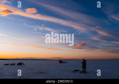 Silhouetten eines Fischers mit Angelrute an einem frostigen Winterabend bei Sonnenuntergang auf dem Fluss Stockfoto