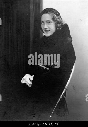 Studio-Porträt einer jungen, schönen Frau in einem Mantel und einer dunklen Baskenmütze, die eine Handtasche unter ihrem Ellenbogen hält. Deutschland. Datum unbekannt, ungefähr 1930er Jahre Stockfoto