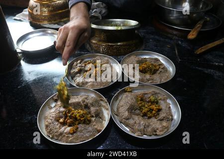 Srinagar Kaschmir, Indien. Januar 2024. Ein Koch garniert Harissa an einem kalten Morgen in Srinagar für Gäste. Harissa ist ein einzigartiges uraltes Hammelrezept, das während der Winter in Kaschmir zubereitet wird. Es ist meistens in den Morgenstunden aus Hammelfleisch, besonders von Schafen, erhältlich. Das Hammelfleisch wird zuerst bei milder Temperatur gekocht und alle Knochen werden extrahiert, um es entbeint zu machen. Das Hammelfleisch wird dann mit Reismehl, Wasser und verschiedenen Gewürzen gemischt und ständig umgerührt, bis es quaschig wird. Die Leute mögen dieses Gericht meistens mit gebackenem Brot. Am 18. Januar 2024 In Srinagar Kaschmir, Indien. (Kreditbild: © Fi Stockfoto