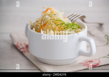 Sauerkraut mit Karotten und Gewürzen in einer weißen Schüssel auf einem hellen Holztisch. Stockfoto