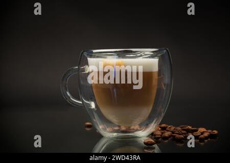 Heißer Kaffee mit Milch in Glasbecher isoliert auf schwarzem Hintergrund Stockfoto