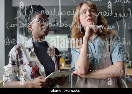 Zwei zweirassige Programmiererinnen schreiben Code auf Glasplatte in modernen IT-Firmenbüros Stockfoto