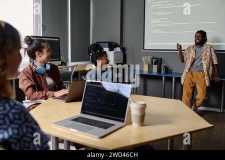 Indischer Mann, der seinen fröhlichen Kollegen vor ihm am Schreibtisch Code auf der digitalen Tafel zeigt Stockfoto