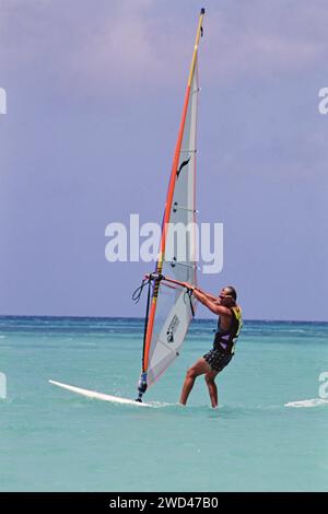 Junger Mann Windsurfen (Boardsegeln) im blauen Wasser vor Aruba CA. Anfang der 1990er Jahre Bitte schreiben Sie dem Fotografen Joan Iaconetti zu Stockfoto