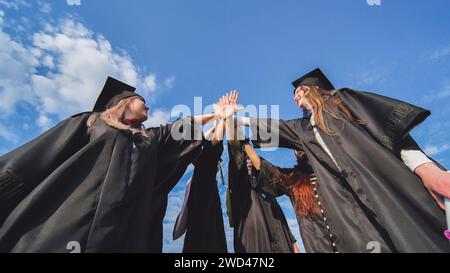 Team von College- oder Universitätsstudenten, die den Abschluss feiern. Gruppe glücklicher erfolgreicher Absolventen in akademischen Hüten und Gewändern, die im Kreis stehen und Stockfoto