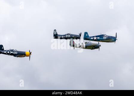 Amerikanische Kampfflugzeuge aus dem 2. Weltkrieg fliegen in enger Formation am Himmel. F4U Corsair, F8F Wildcat, F4F u. a. Stockfoto