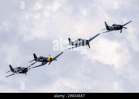 Amerikanische Kampfflugzeuge aus dem 2. Weltkrieg fliegen in enger Formation am Himmel. F4U Corsair, F8F Wildcat, F4F u. a. Stockfoto