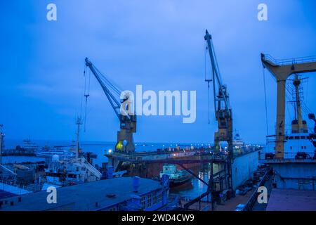 Industriewerft in der Dämmerung, schwimmendes Trockendock mit Schiff in Reparatur, Kräne in Bereitschaft. Wartung von Seeschiffen, Nachthimmel, schwere Maschinen Stockfoto