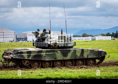 T72 Tank (M4 CZ Variantennummer 029) fährt während einer Demonstrationsübung auf einem schlammigen Feld vor NATO- und Tschechischen Flaggen. Stockfoto