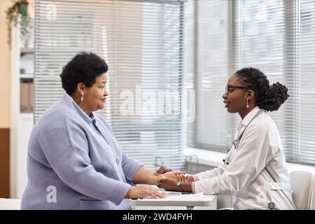 Fröhlicher Arzt, der Patienten mit Pulskontrolle von Hand überprüft Stockfoto