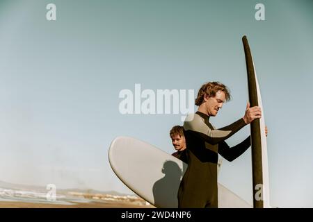 Gruppe von Freunden Surfer in Neoprenanzügen, die mit Surfbrettern stehen und sich auf den Wellenritt vorbereiten Stockfoto